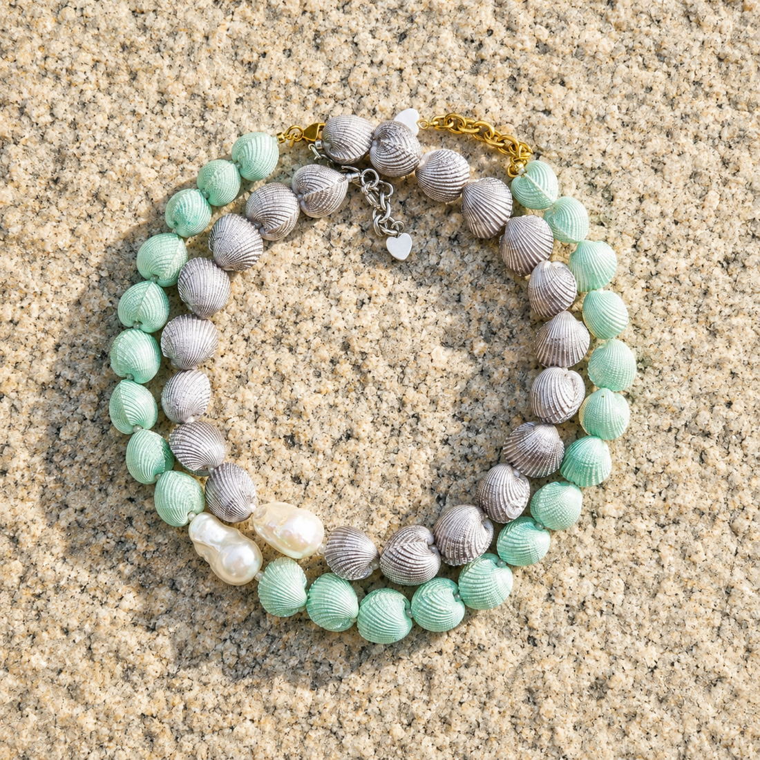 Mint and gray shell necklaces from LUMÉA by HANAÉ styled together on natural stone in sunlight