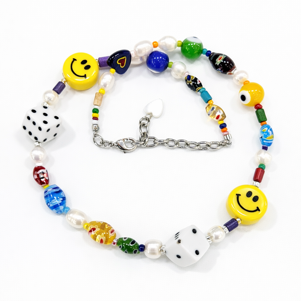 Close-up detail of HANAÉ Lucky Mood Charm Necklace showing colorful Venetian glass beads, yellow smiley charms, dice beads, freshwater pearls, and mixed textures.