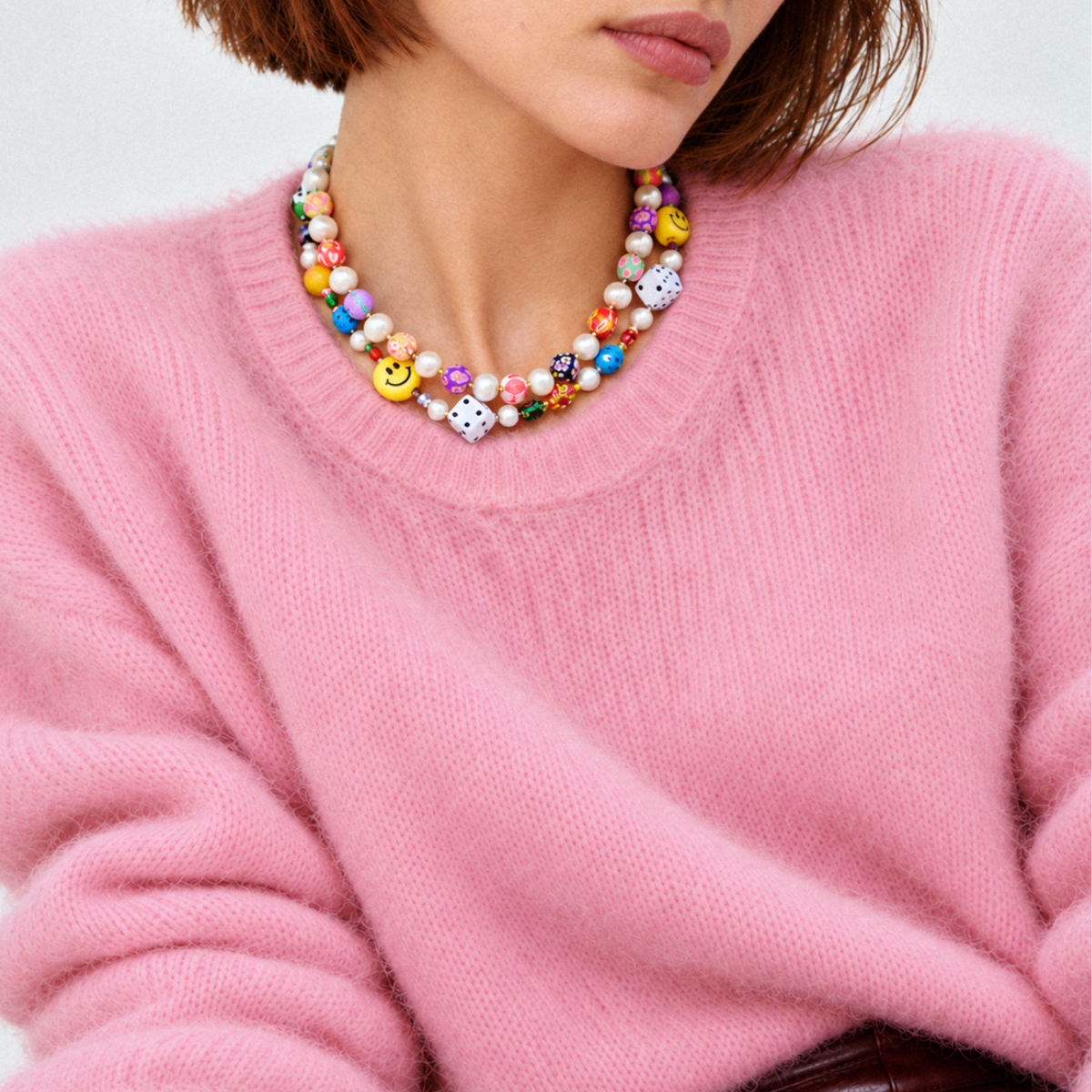 HANAÉ Lucky Mood Charm Necklace featuring colorful Venetian glass beads, playful smile and dice beads, and freshwater pearls, styled with a soft pink knit sweater for fall and winter.