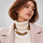 Model wearing LUMÉA Amberwood Baroque Necklace featuring brown wood beads and baroque pearls, styled with a cream knit sweater and beige coat for fall and winter