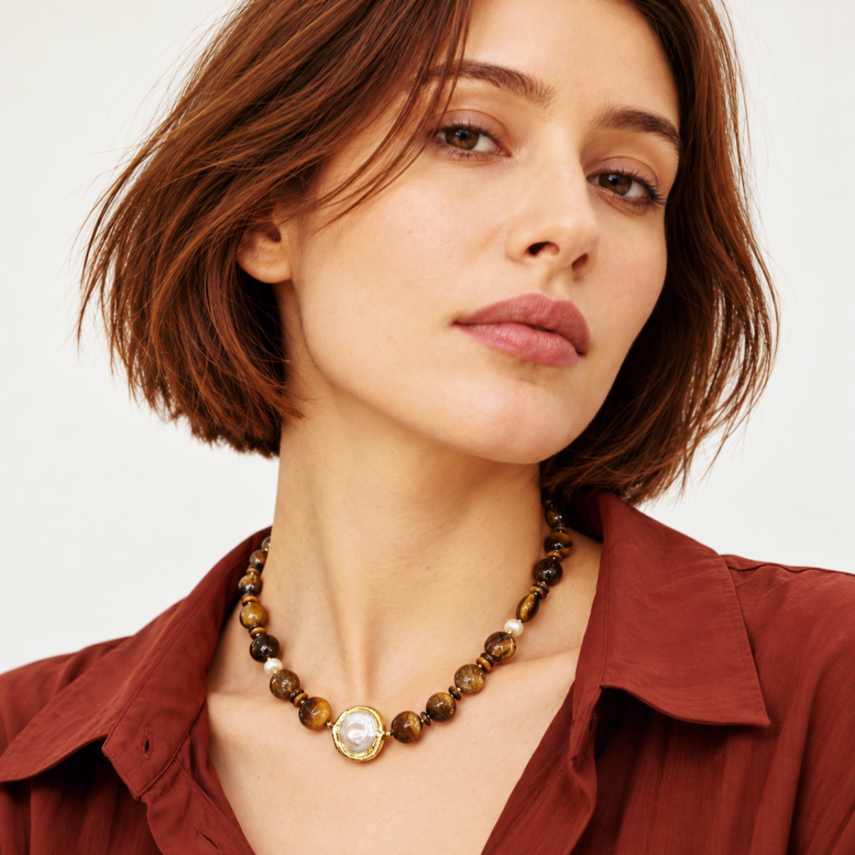 LUMÉA handcrafted tiger eye gemstone necklace with freshwater pearl accents, styled with a rust brown shirt on a female model.
